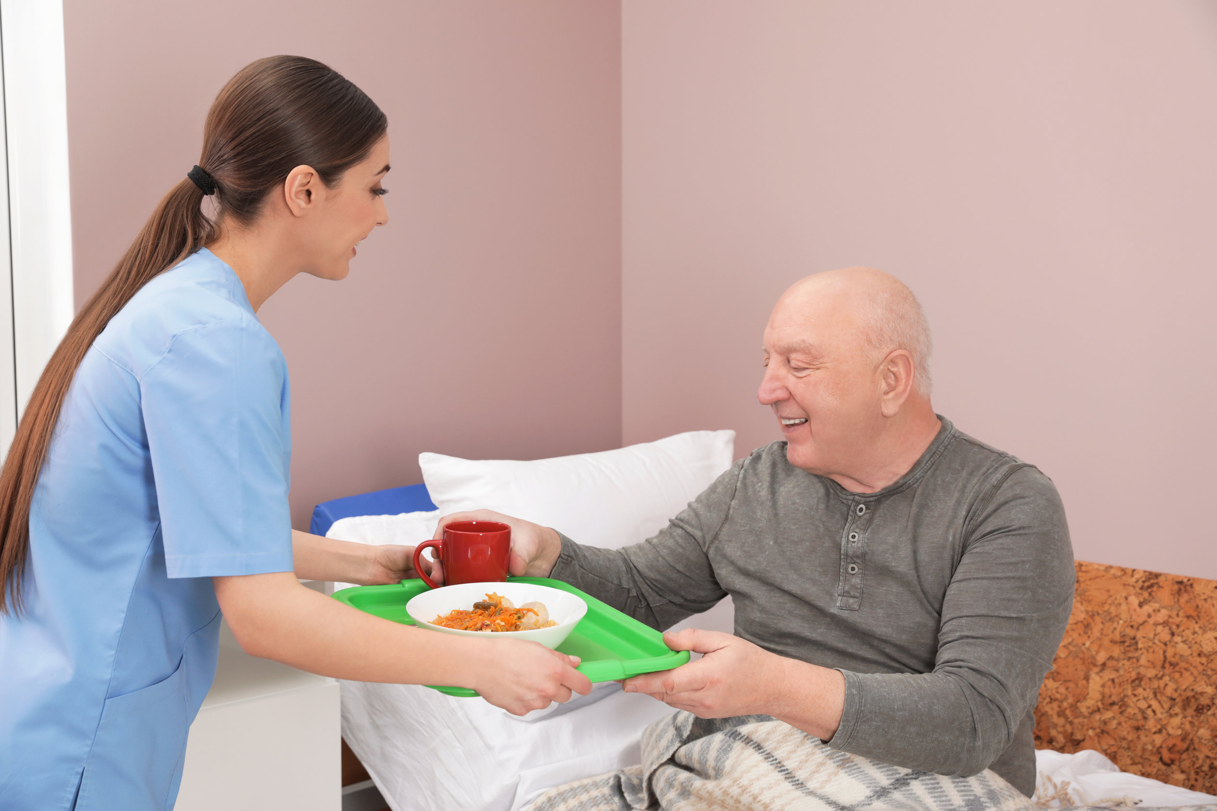Nurse giving tray with food to senior patient in hospital ward. Medical assisting
